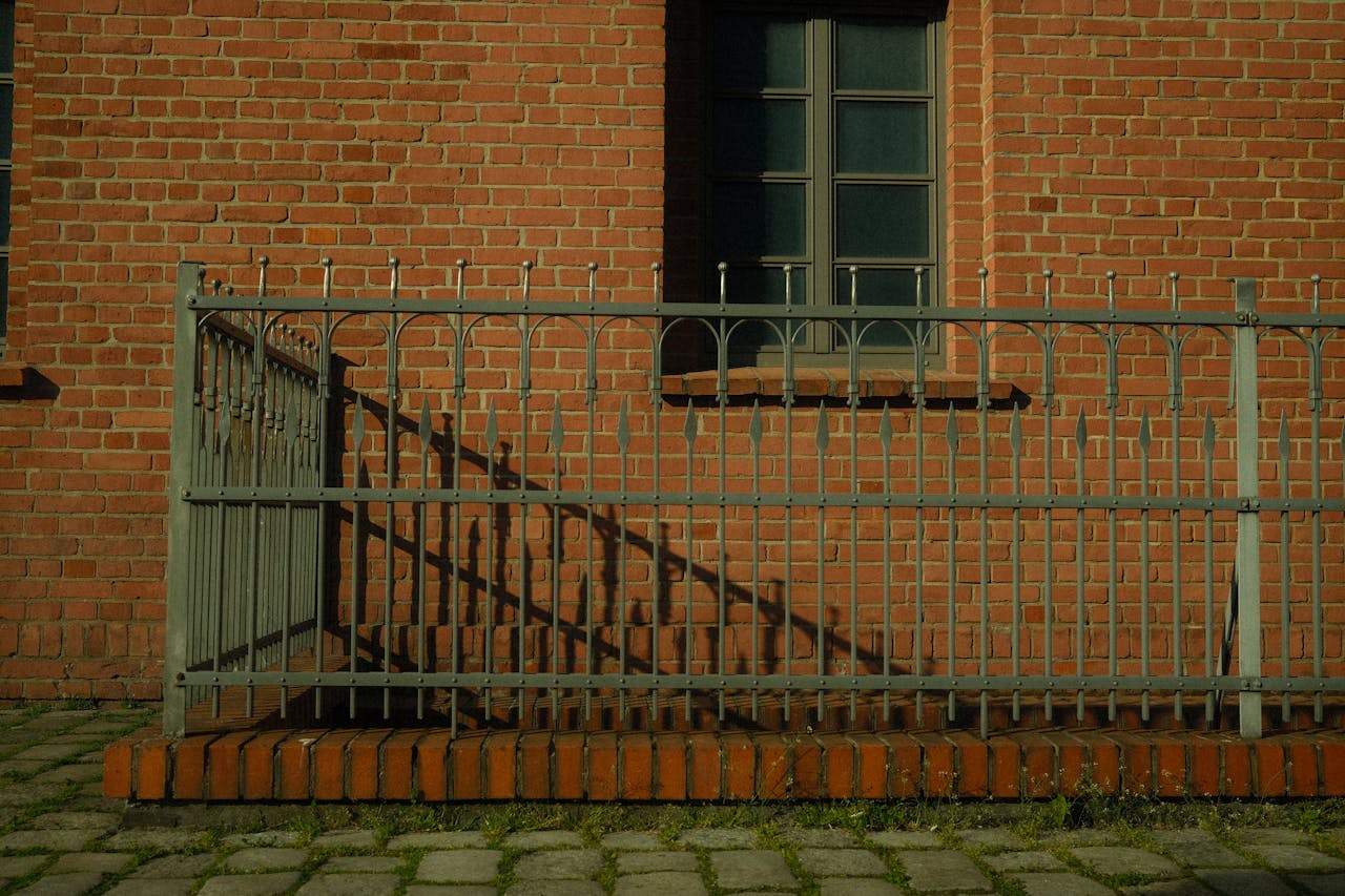 Close-up of a brick wall with decorative metal railings casting shadows in daylight.